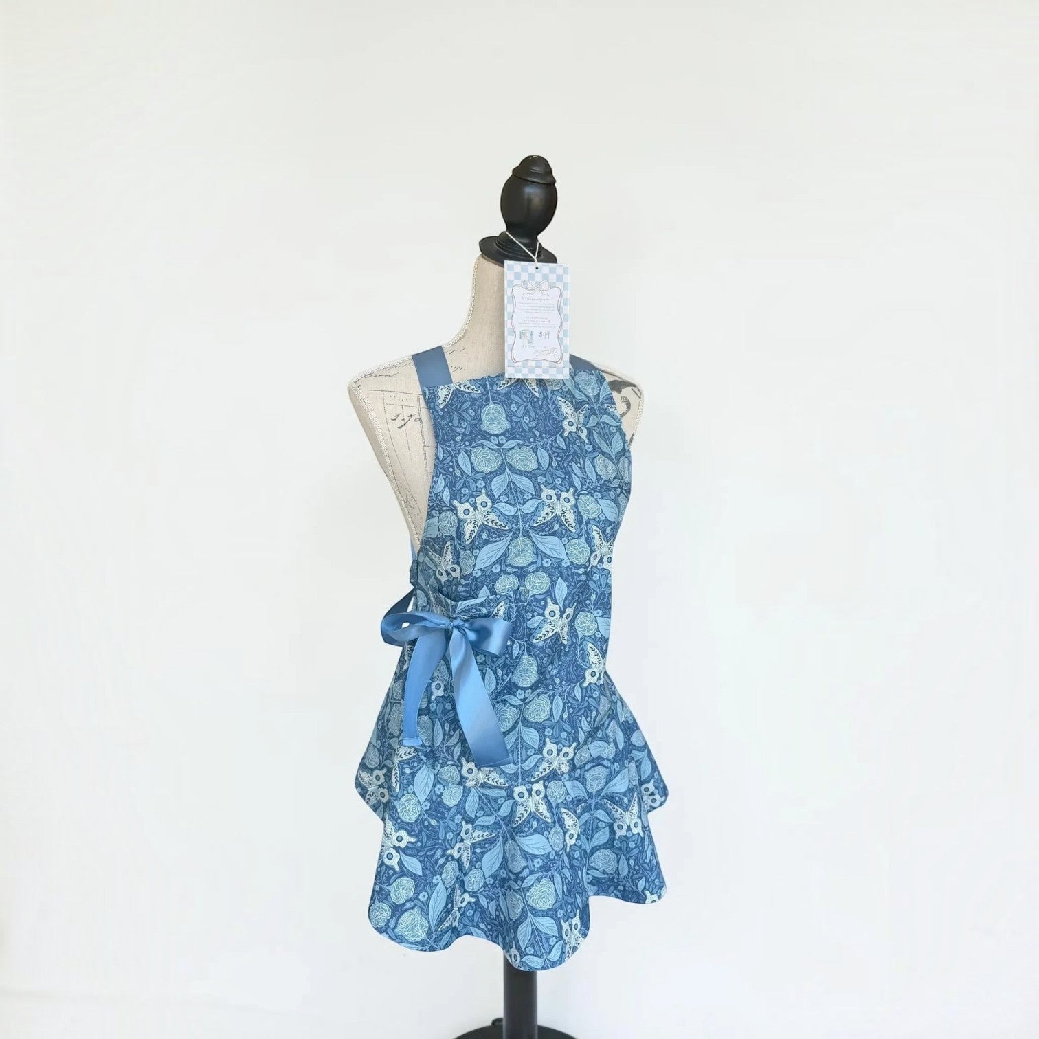 Her Good Eye blue floral print kitchen apron with satin ribbon side bow on a mannequin
