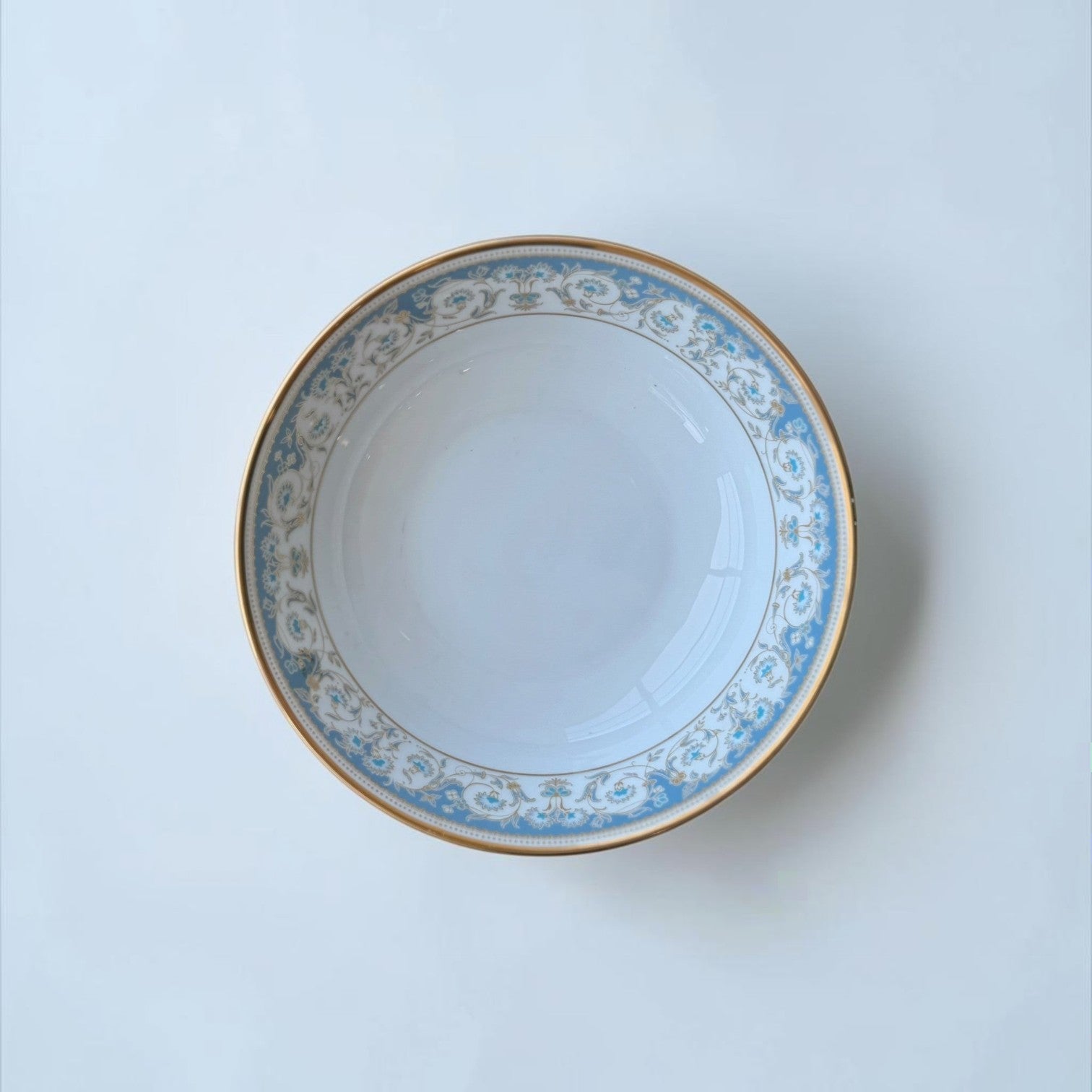 Her Good Eye decorative porcelain serving bowl with blue floral pattern and gold rim.