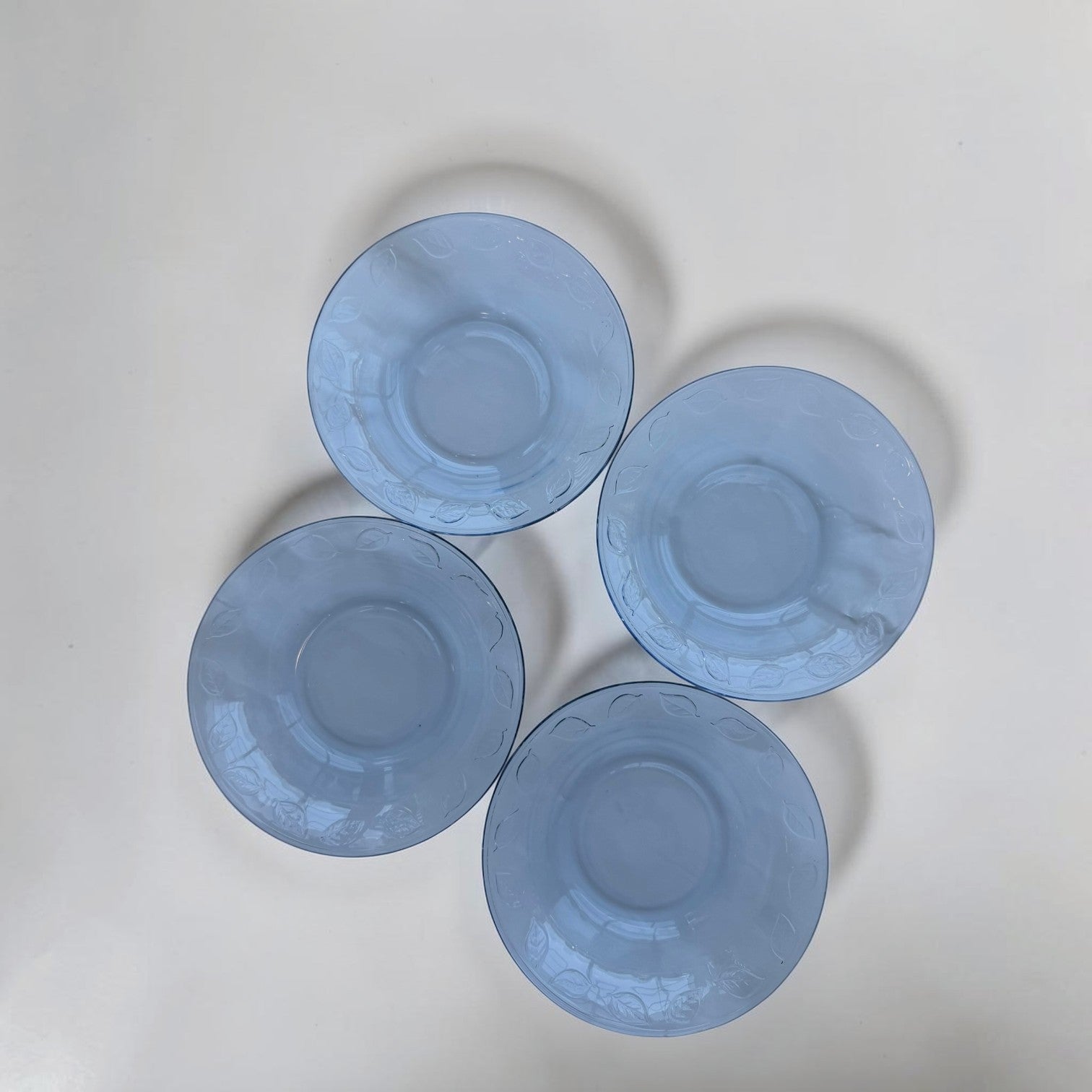 Her Good Eye set of four blue glass dessert plates with embossed leaf pattern around the rim.