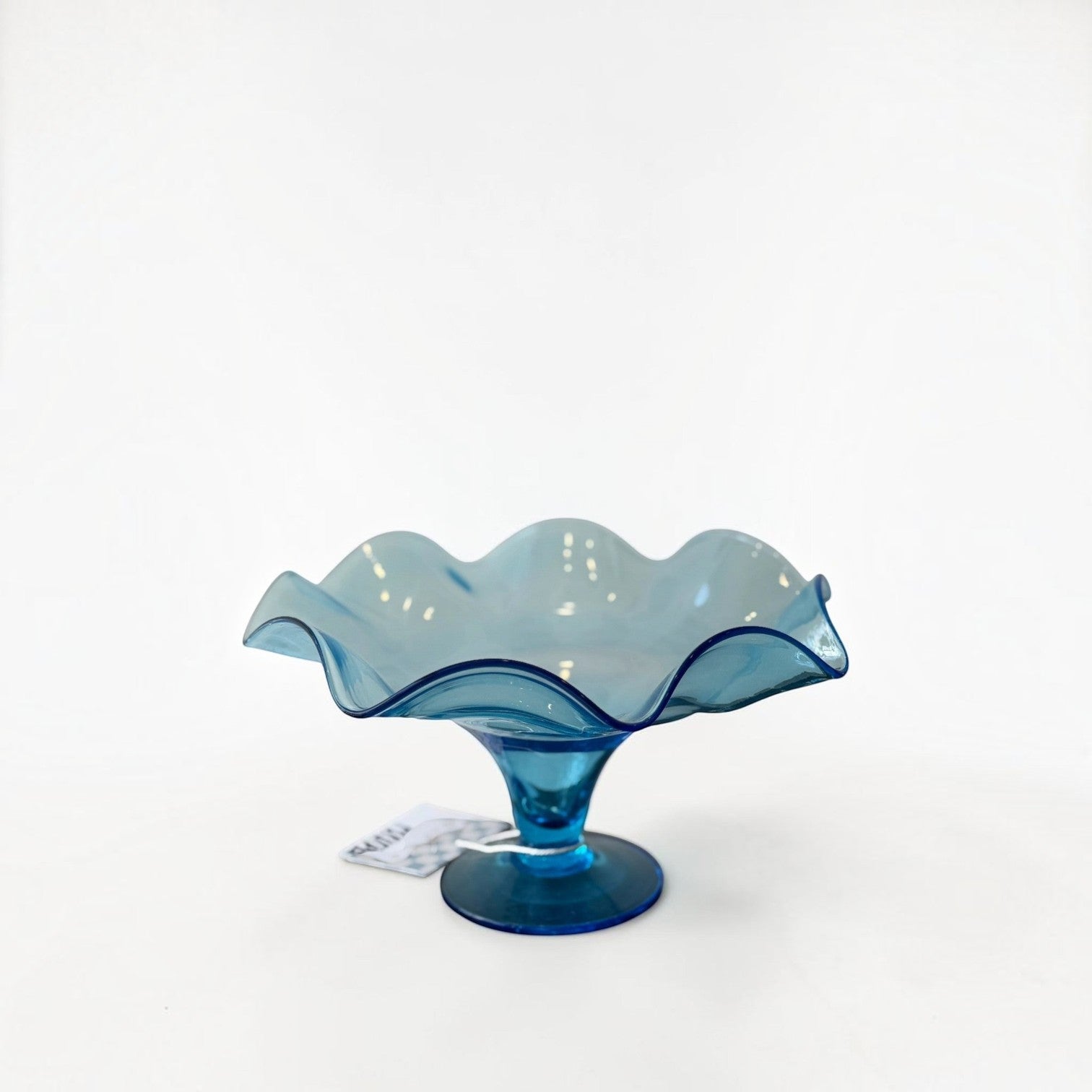 Her Good Eye vintage blue glass pedestal bowl with a decorative scalloped ruffled edge on a white background