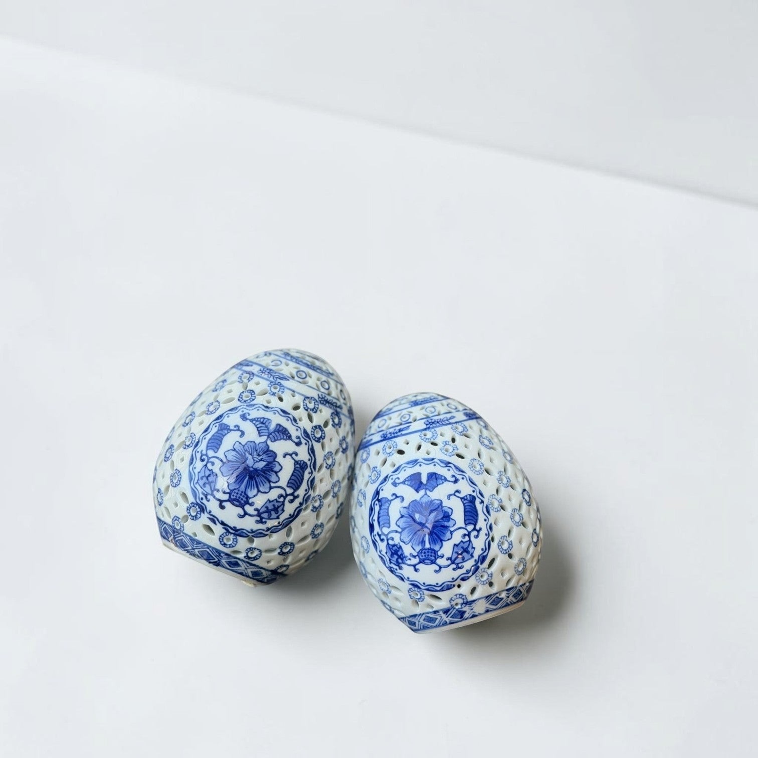 Her Good Eye pair of blue and white porcelain decorative eggs with intricate cut-out floral designs.