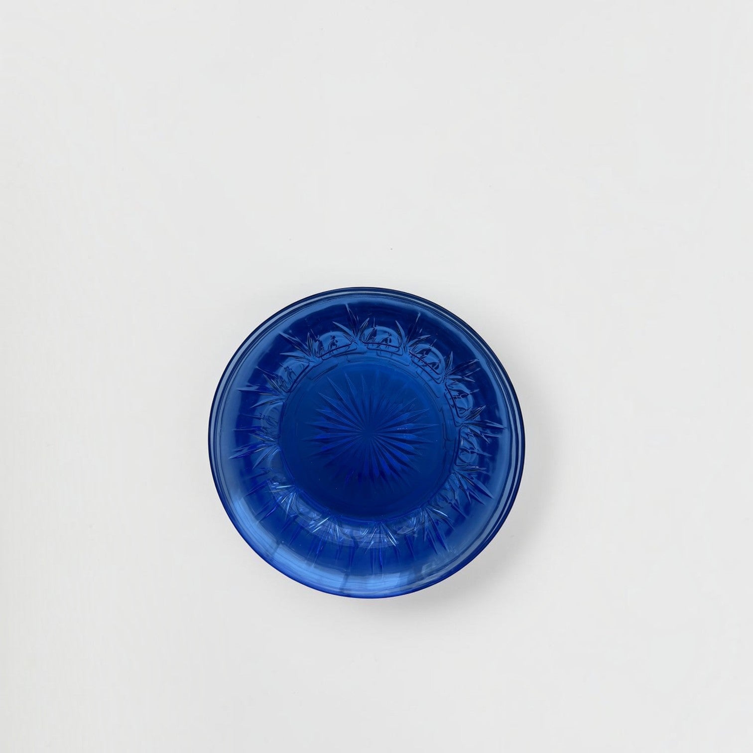 Her Good Eye vintage cobalt blue pressed glass dessert plate with a starburst center and geometric rim pattern.