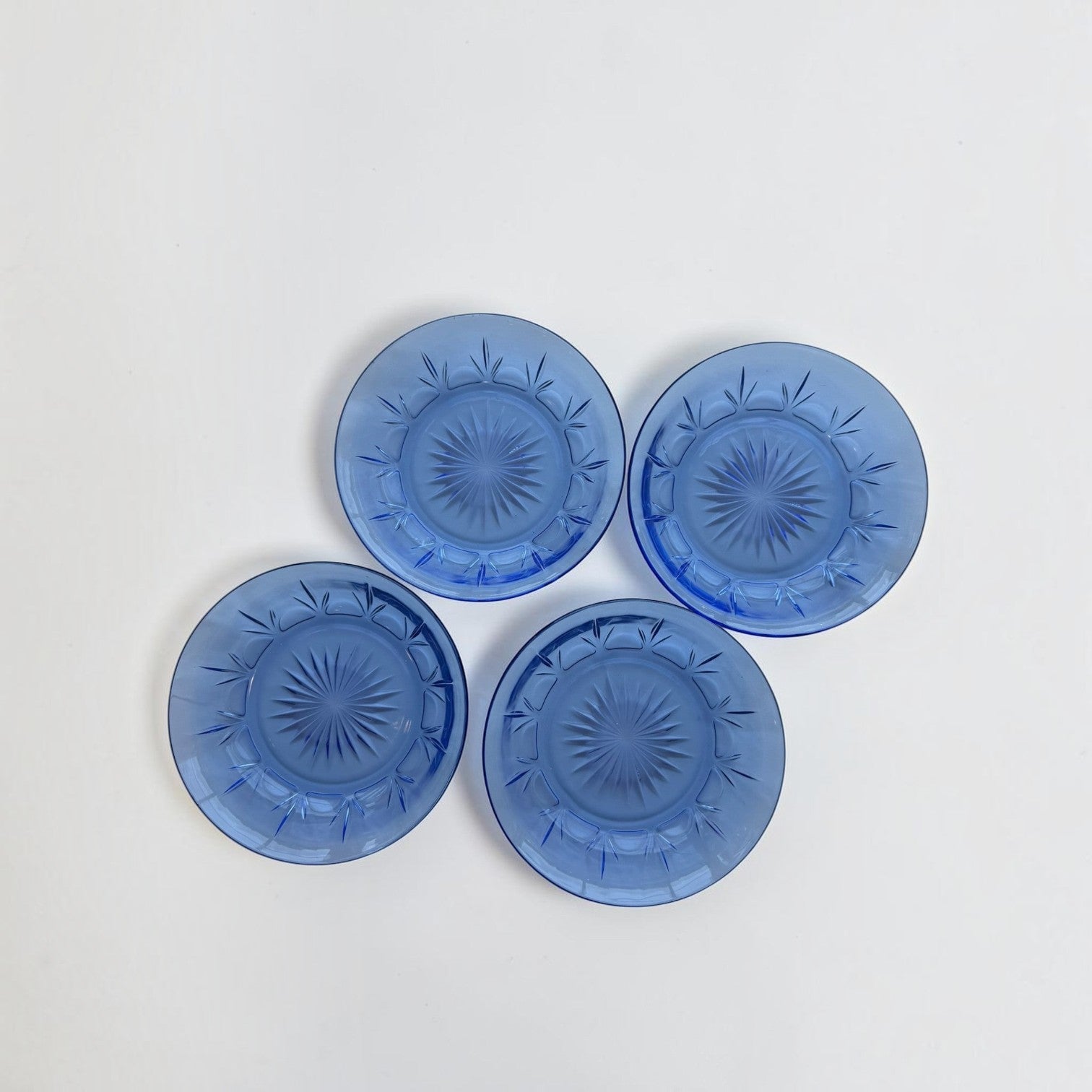 Her Good Eye set of four vintage-style cobalt blue pressed glass dessert plates with intricate starburst patterns.