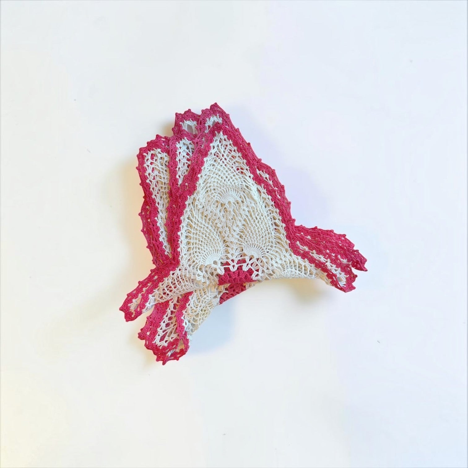 Her Good Eye handmade crochet doily with intricate white lace and a vibrant pink border in a star-like silhouette.