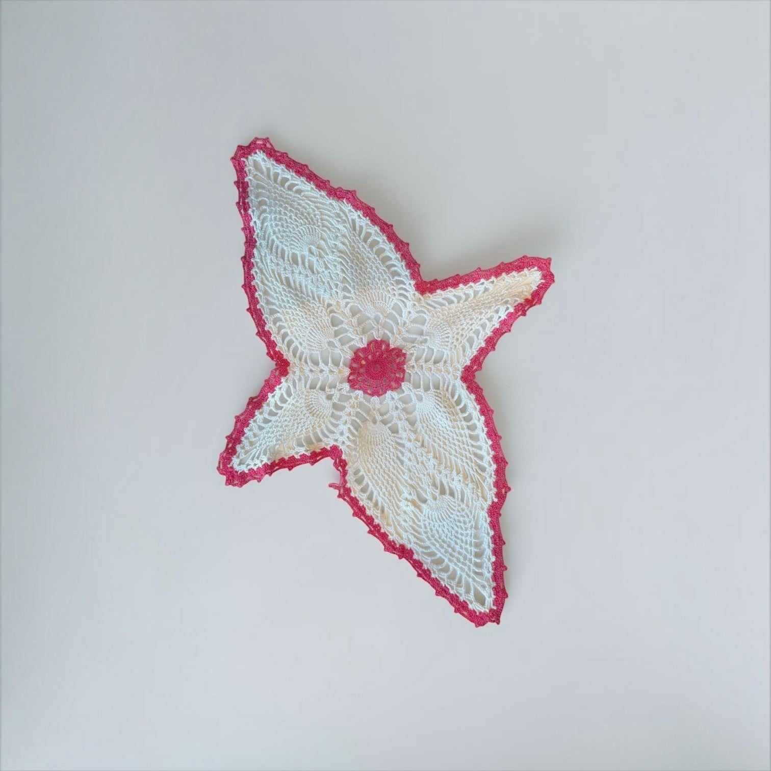 Her Good Eye handmade white crochet doily with a vibrant pink star-shaped border and intricate lace detailing.