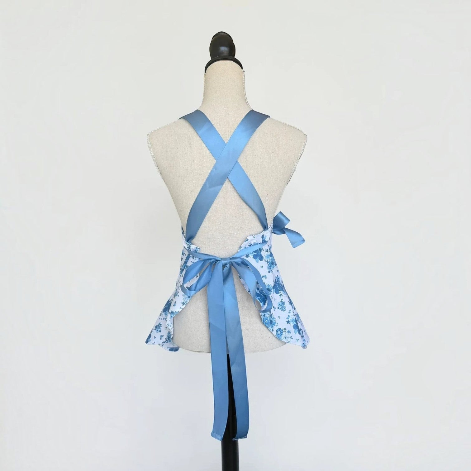 Her Good Eye floral kitchen apron with blue satin ribbon ties and ruffled hem on a mannequin, back view.