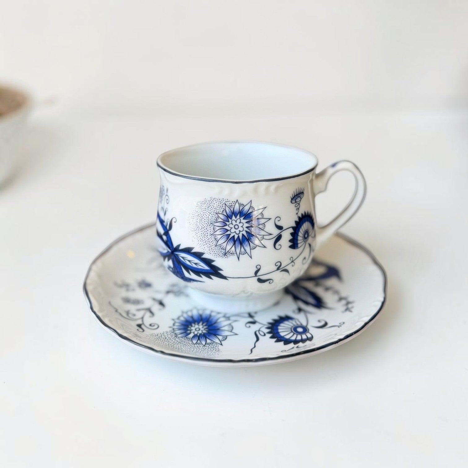 Her Good Eye blue and white floral ceramic teacup and saucer set with scalloped edges and black trim.