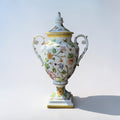 Her Good Eye decorative white ceramic urn with lid, hand-painted with colorful floral motifs and gold trim.