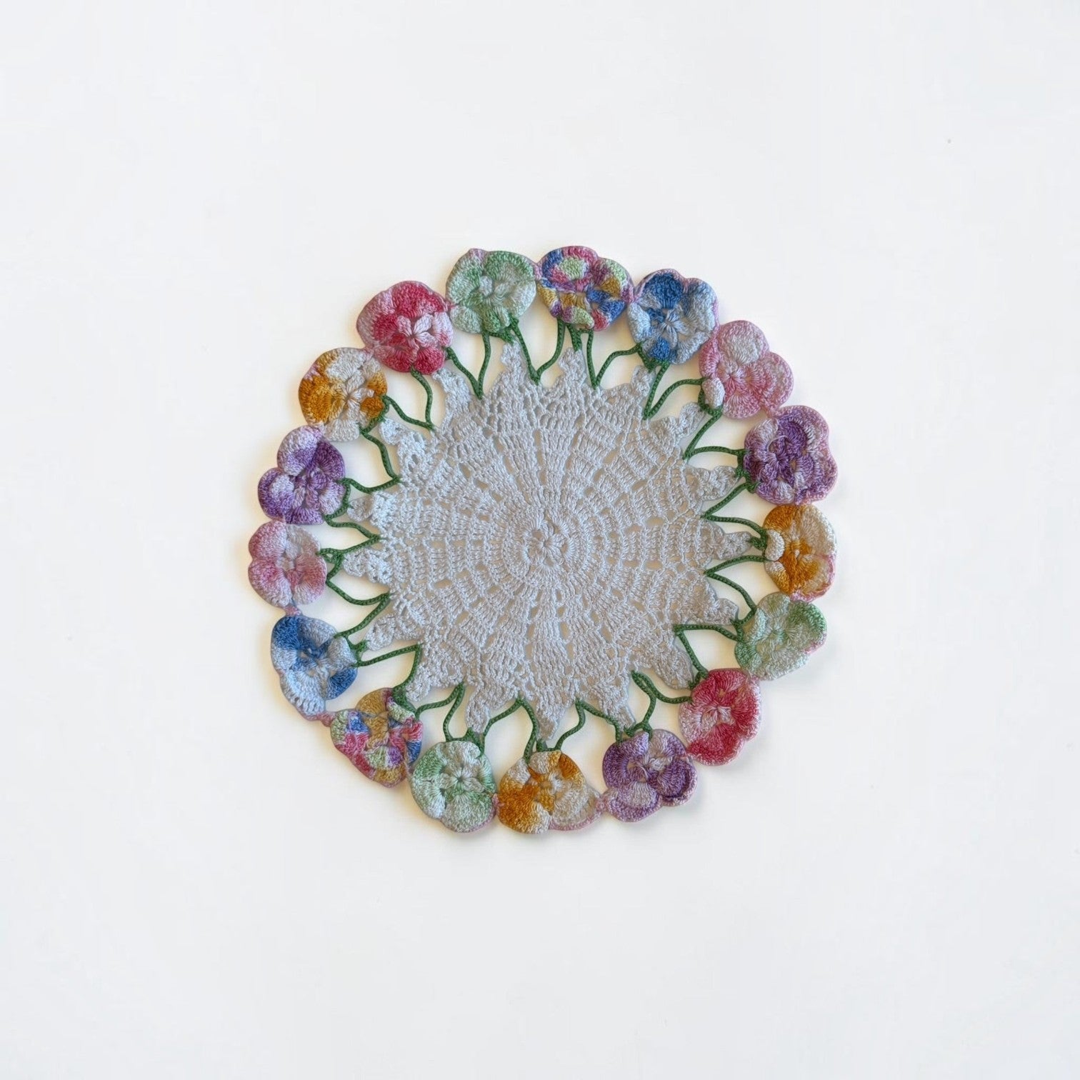 Her Good Eye handmade crochet doily with a neutral center and a border of multicolored pansy flowers.