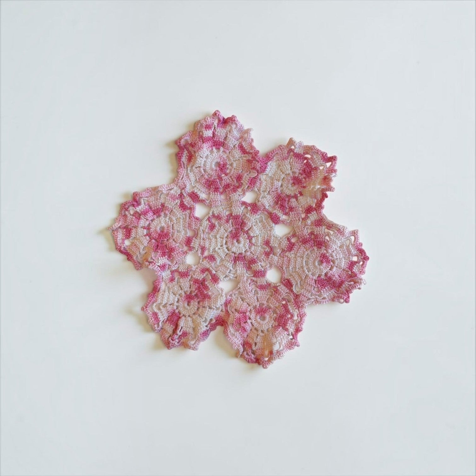 Her Good Eye handmade crochet doily in variegated pink and white yarn with an intricate floral openwork design.