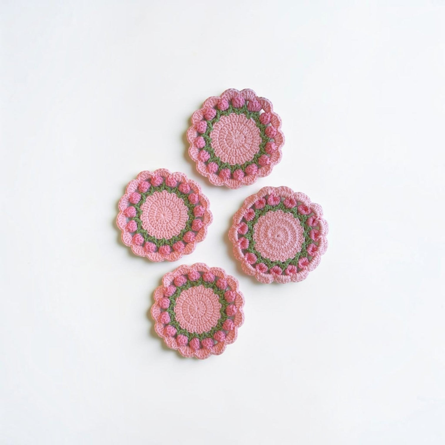 Her Good Eye handmade crochet floral coasters in pastel pink and green with intricate stitch work on a white background.