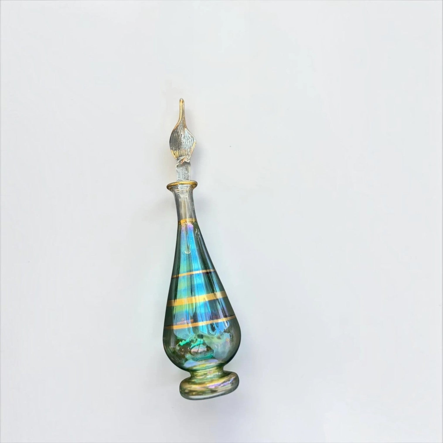 Her Good Eye iridescent glass perfume bottle with gold stripes and a tapered stopper on a white background.