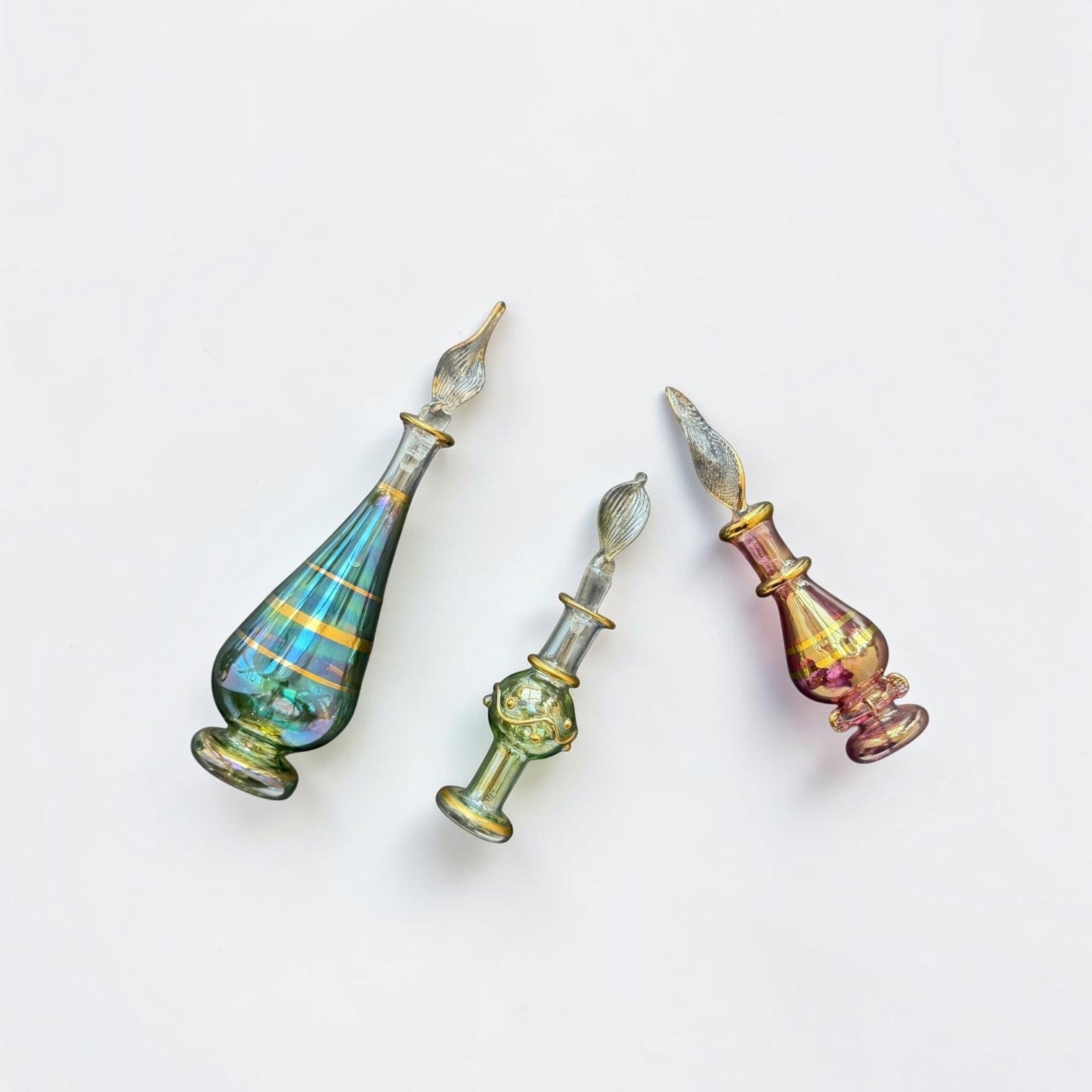 Her Good Eye iridescent hand blown glass perfume bottles in teal, sage, and magenta with gold-tone vintage detailing.