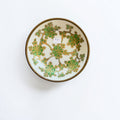 Her Good Eye decorative porcelain bowl featuring green floral patterns and gold accents with a brass-toned metal rim.