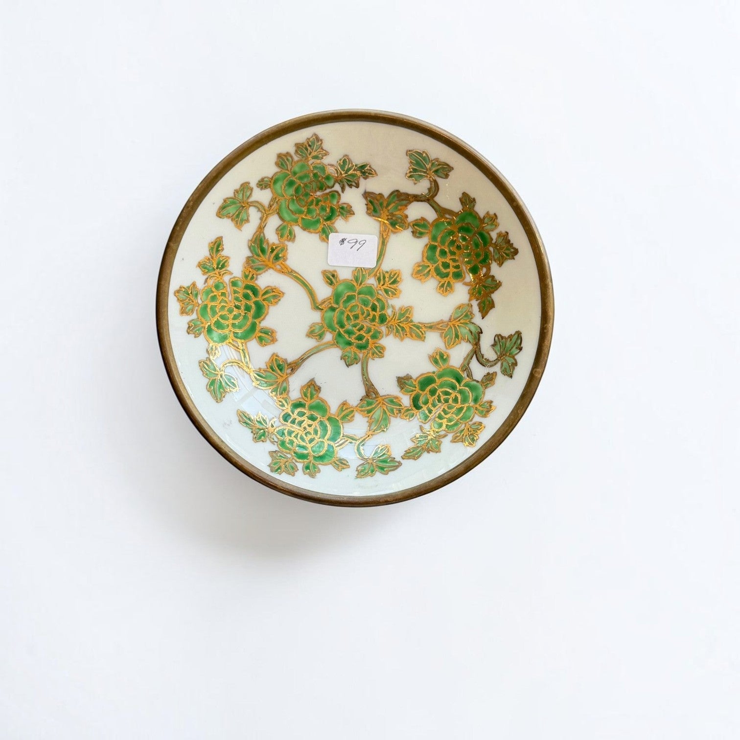 Her Good Eye decorative porcelain bowl featuring green floral patterns and gold accents with a brass-toned metal rim.