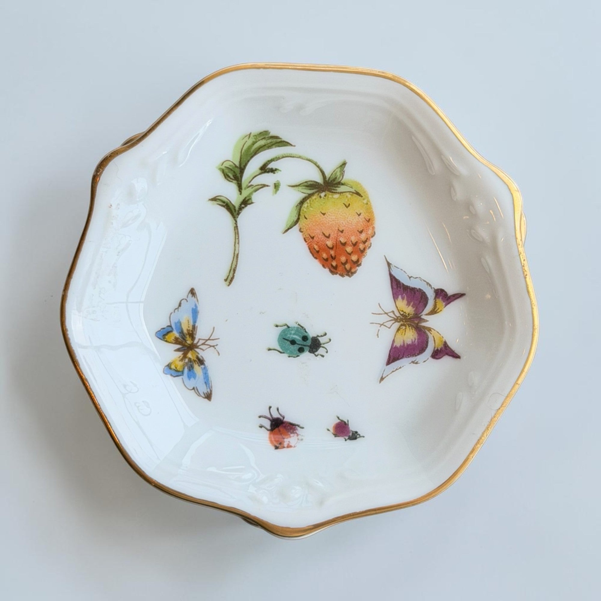 Her Good Eye white porcelain trinket dish with gold rim, strawberry, butterfly, and ladybug botanical illustrations.
