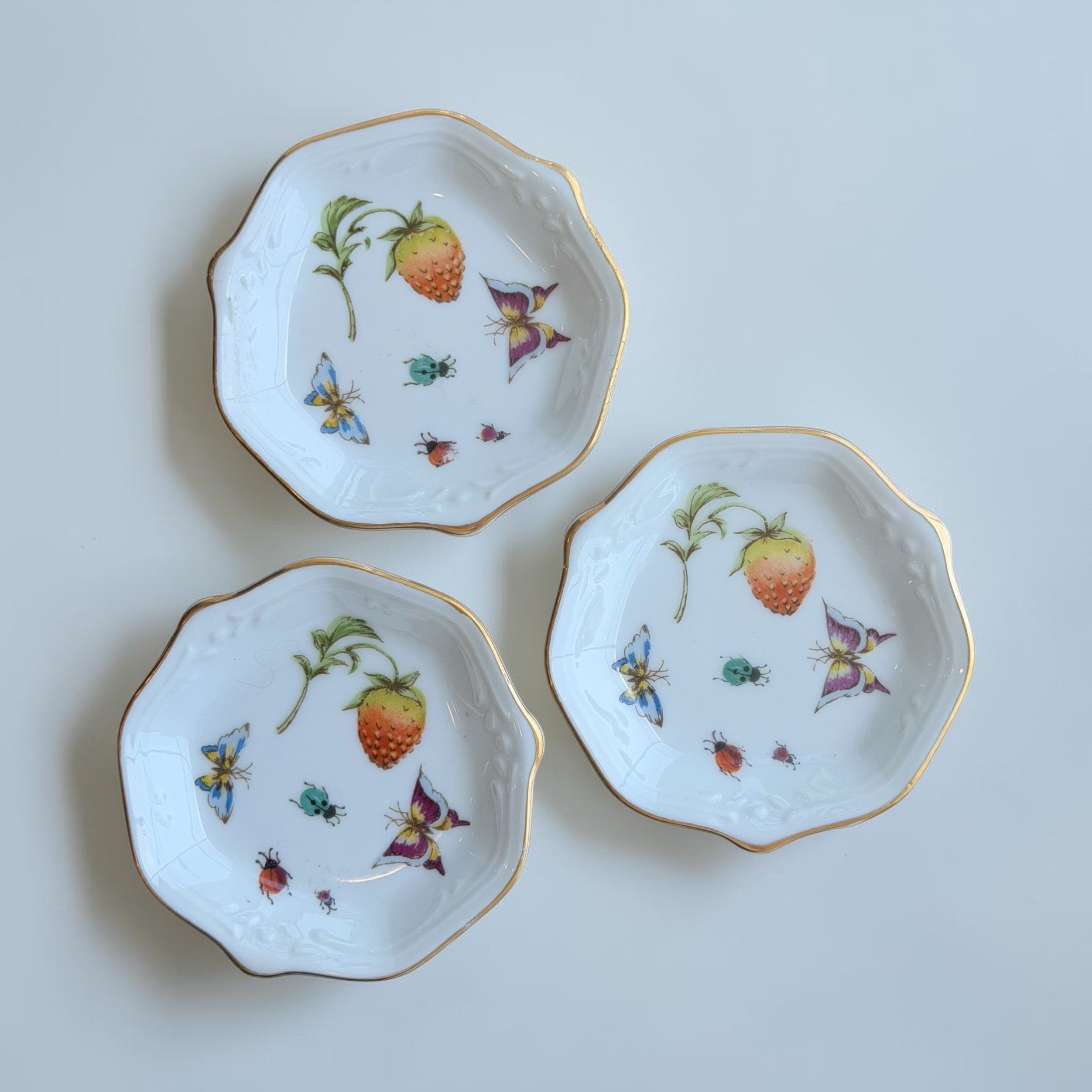 Her Good Eye porcelain trinket dishes with gold rims, strawberry, butterfly, and ladybug botanical illustrations.