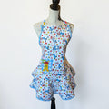 Her Good Eye quilted kitchen apron with multi-colored cartoon character print, blue gingham pocket, and ruffle skirt.