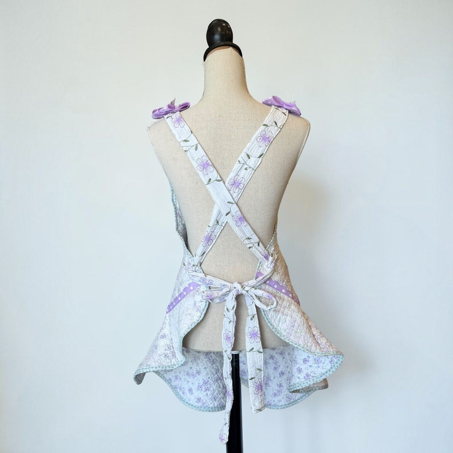 Her Good Eye quilted floral patchwork kitchen apron with lavender bows and cross-back straps on a mannequin