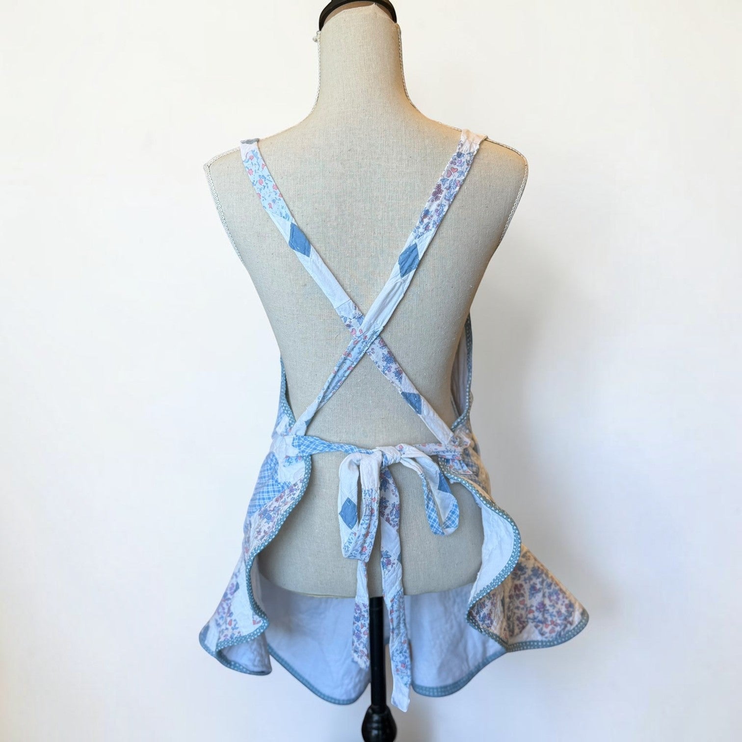Her Good Eye quilted kitchen apron featuring a blue and white patchwork heart pattern with floral and gingham details.