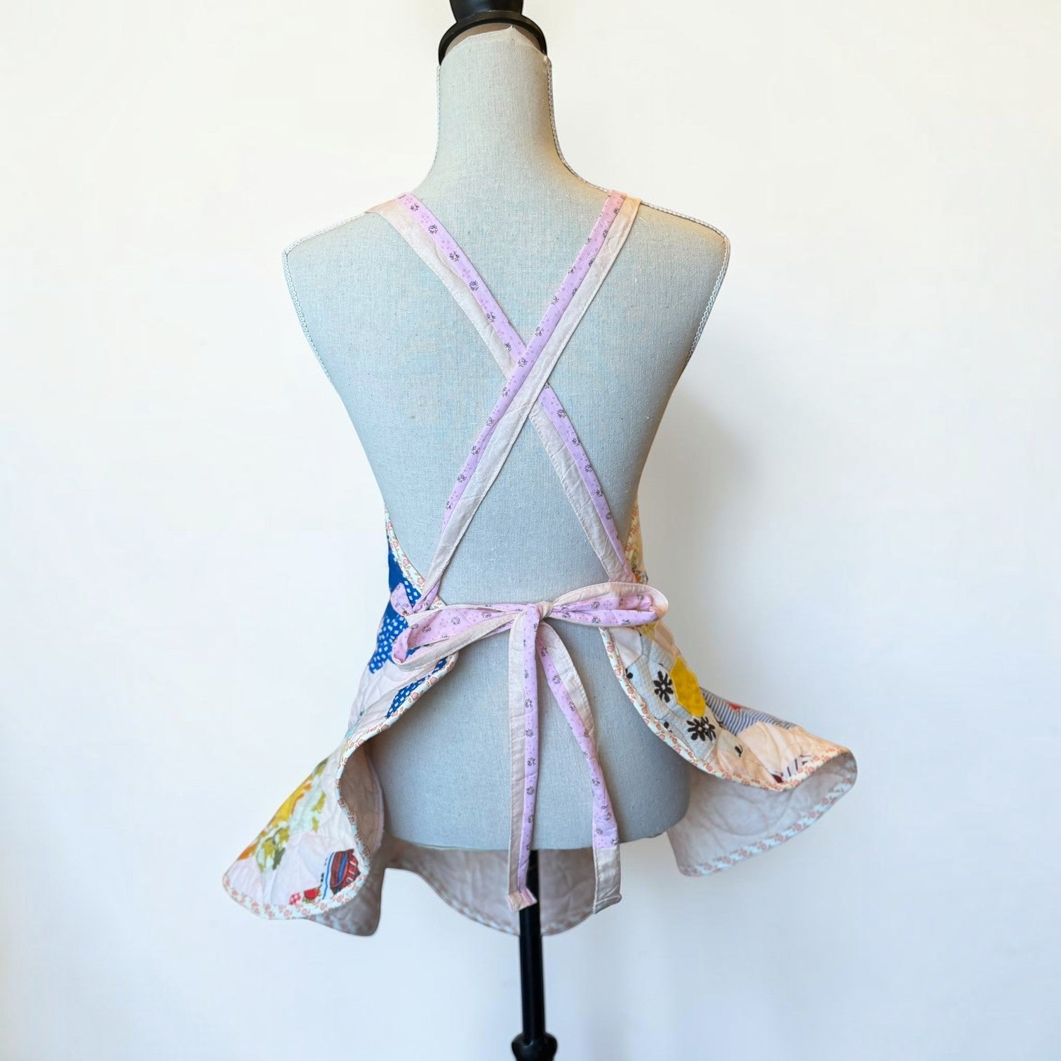 Back view of a Her Good Eye handmade quilted patchwork apron with floral and gingham hexagon motifs on a mannequin.