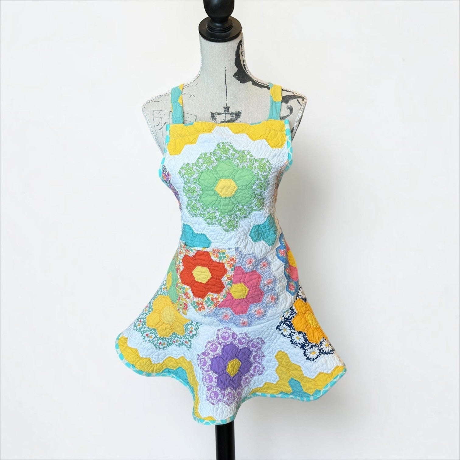 Her Good Eye handmade quilted patchwork apron with vibrant floral hexagon patterns in yellow, green, orange, and purple.