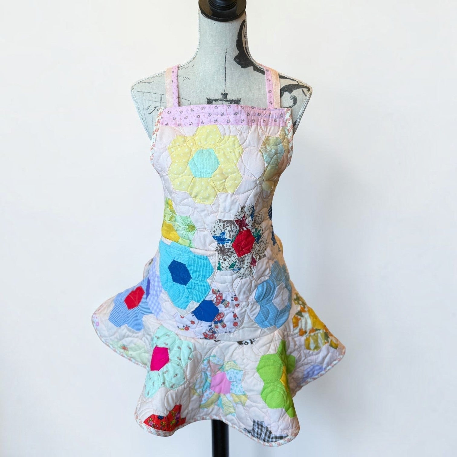 Her Good Eye handmade quilted patchwork apron featuring colorful hexagon fabric motifs in floral and gingham patterns.