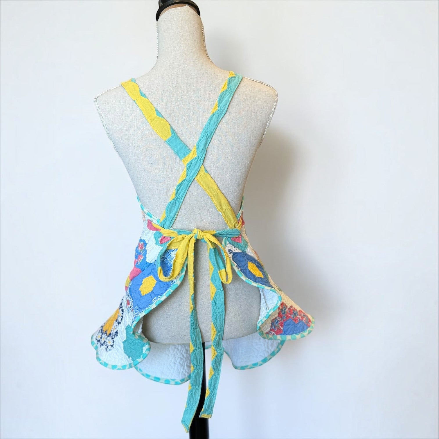 Her Good Eye handmade quilted patchwork apron with yellow and teal straps and a vibrant floral hexagon pattern.