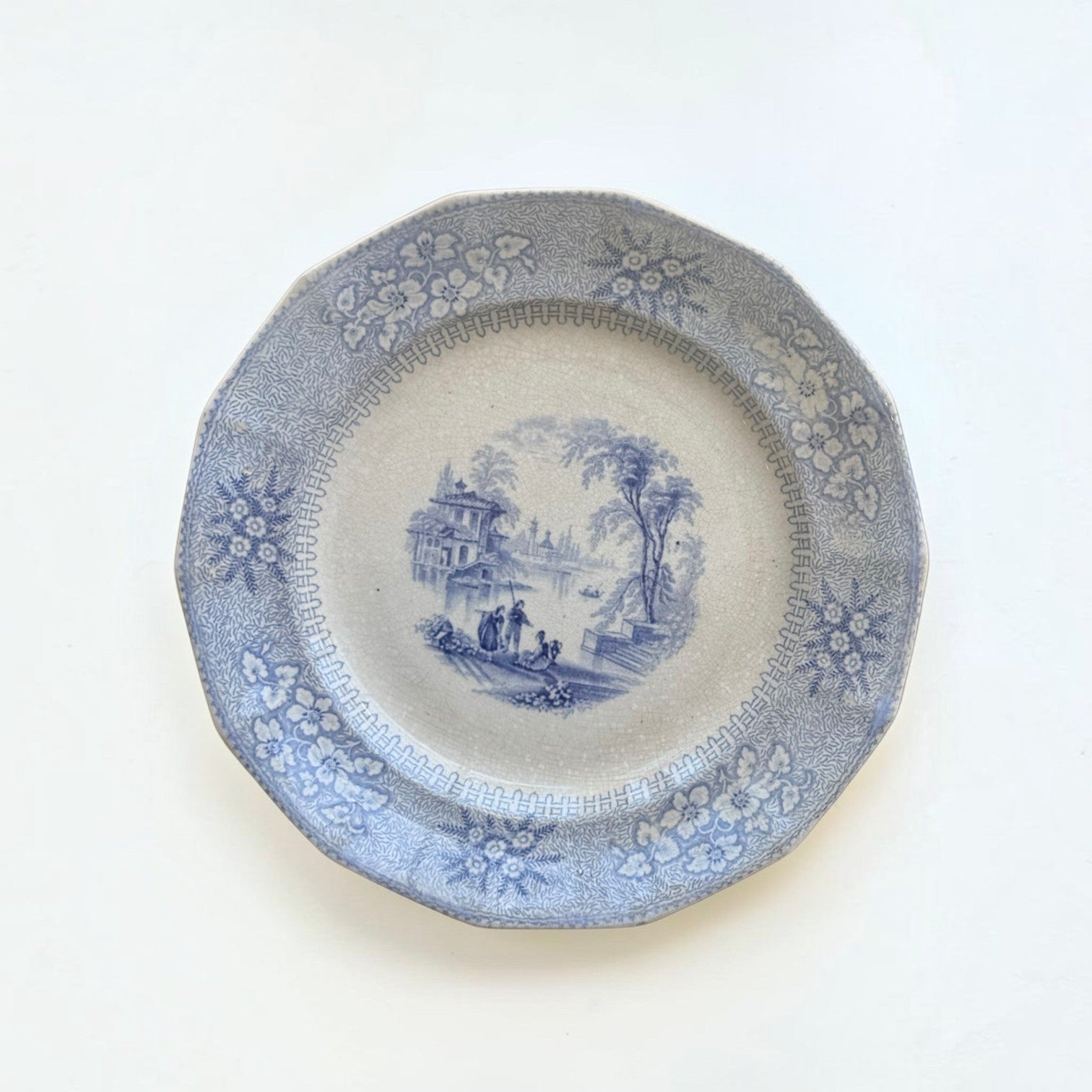 Her Good Eye vintage ceramic dinner plate with blue and white pastoral transferware, floral border, and scalloped edge.