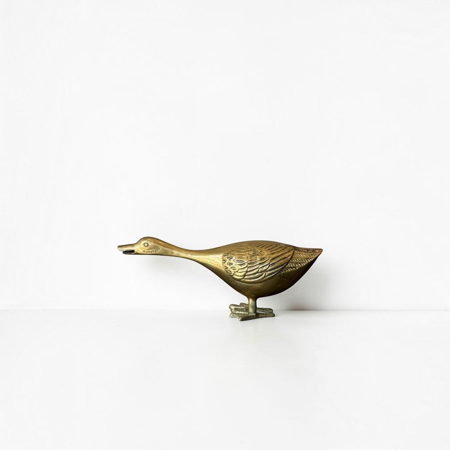 Her Good Eye vintage brass duck figurine with detailed wing carvings and a warm golden patina on a white background.
