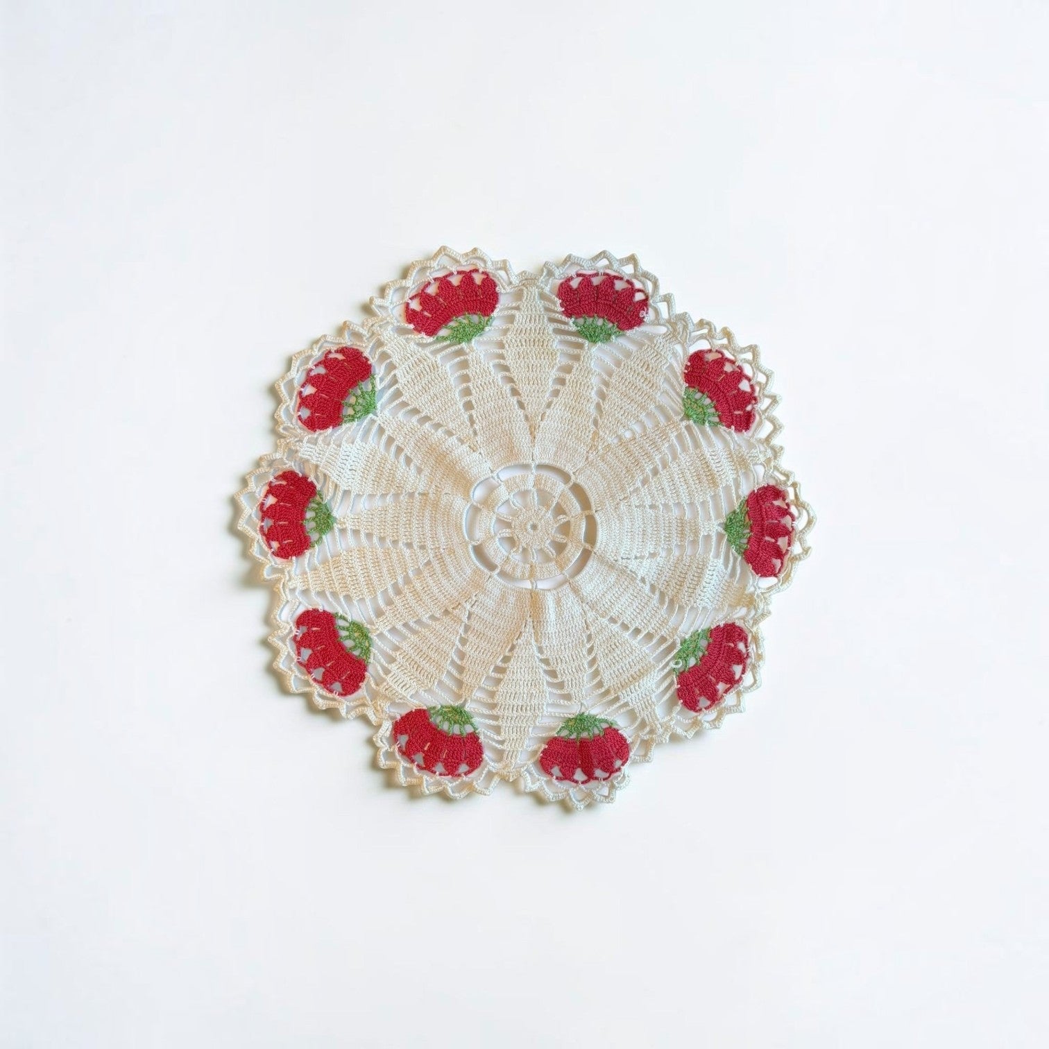 Her Good Eye vintage cream crochet doily with intricate lace, red floral motifs, and green stems on a white background.