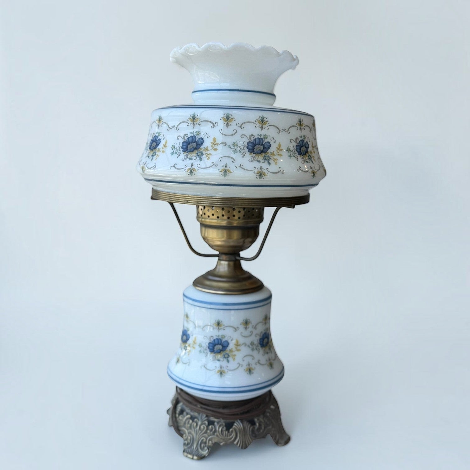 Her Good Eye vintage milk glass hurricane lamp with blue floral patterns, ruffled shade, and antique brass base.