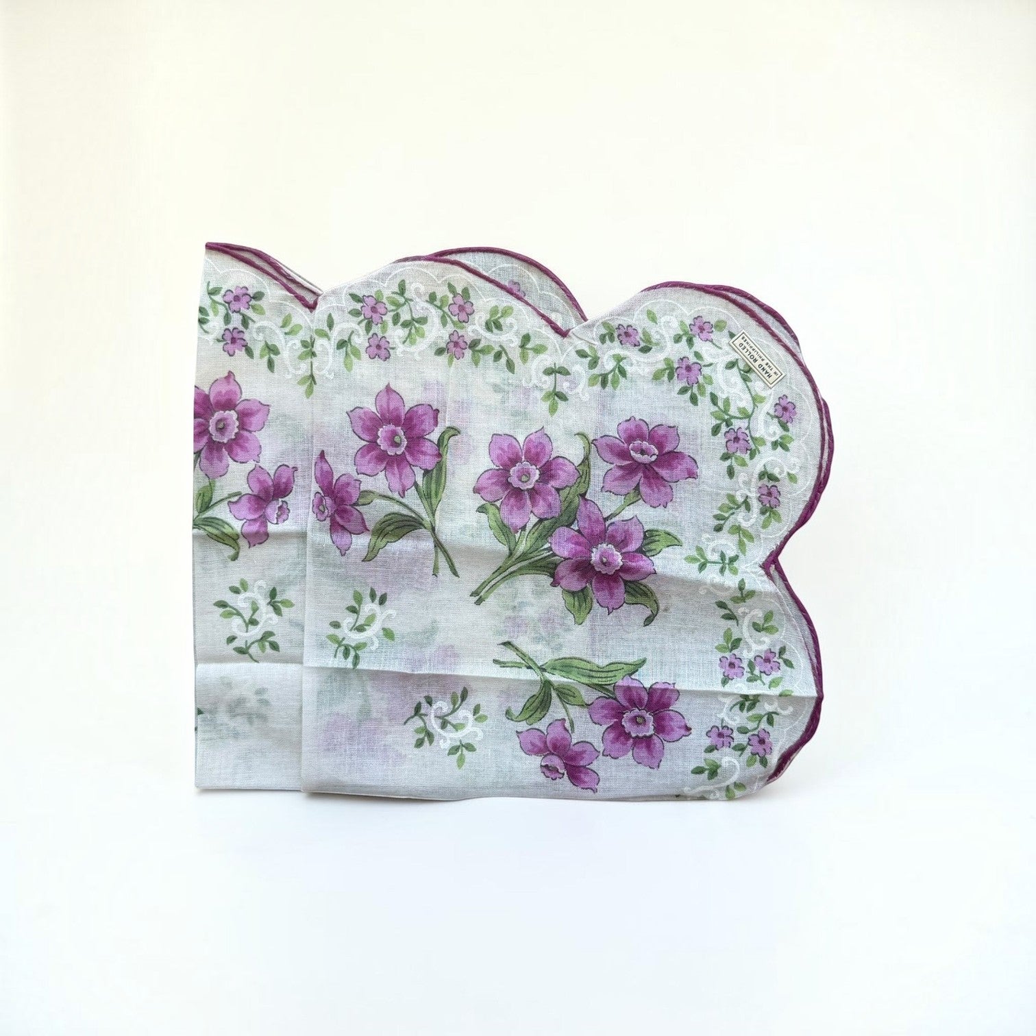 Her Good Eye vintage handkerchief with purple floral print, green foliage, and scalloped edges with a purple hem.