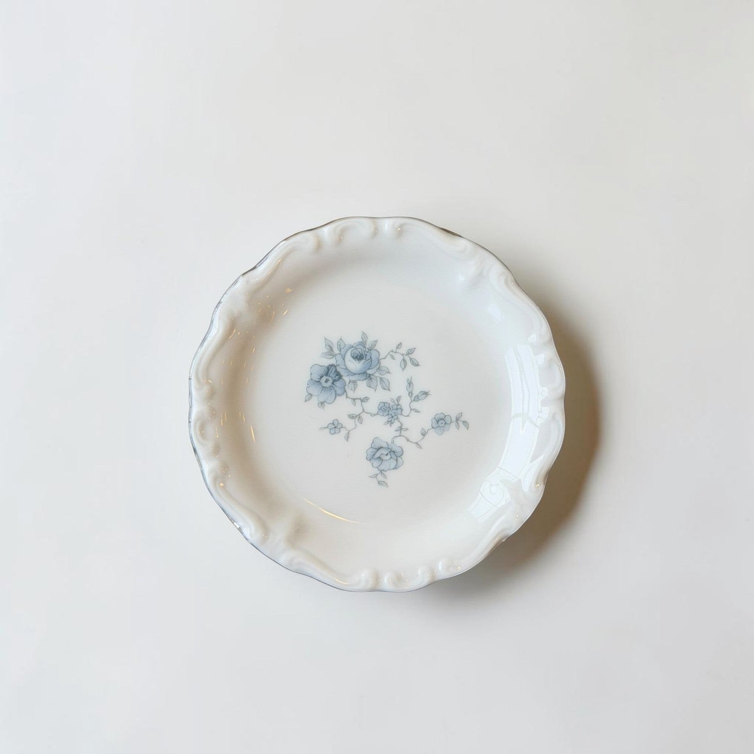 Her Good Eye vintage porcelain bread plate with white base, blue floral motif, and elegant scalloped edges.
