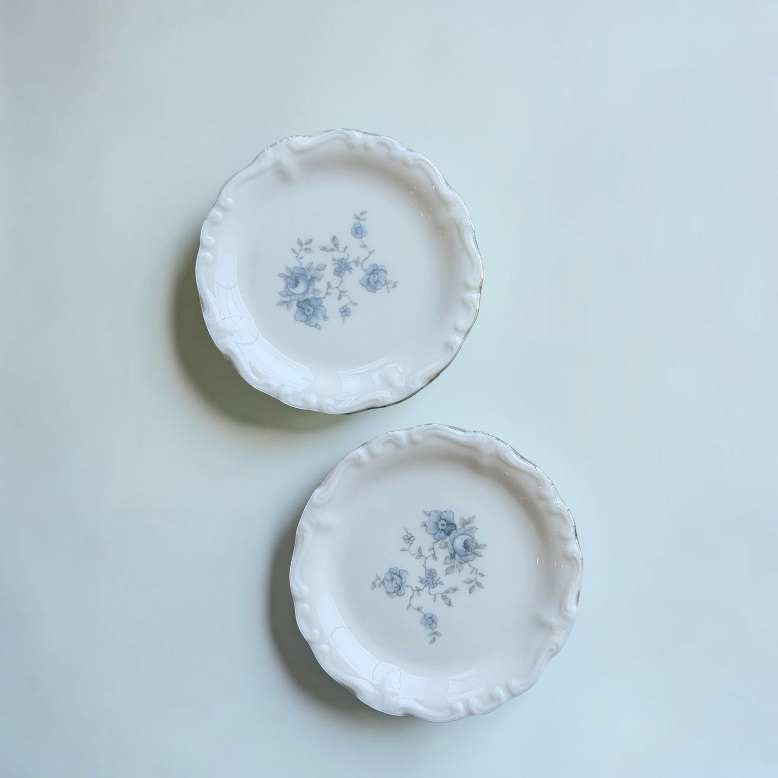 Her Good Eye vintage porcelain bread plates with white base, blue floral pattern, and elegant scalloped edges.